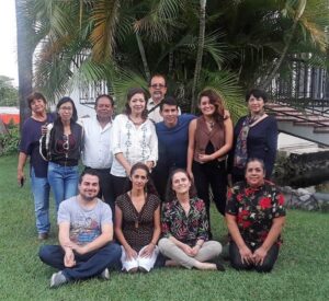 Group photo of eleven people posing outdoors by palm trees.